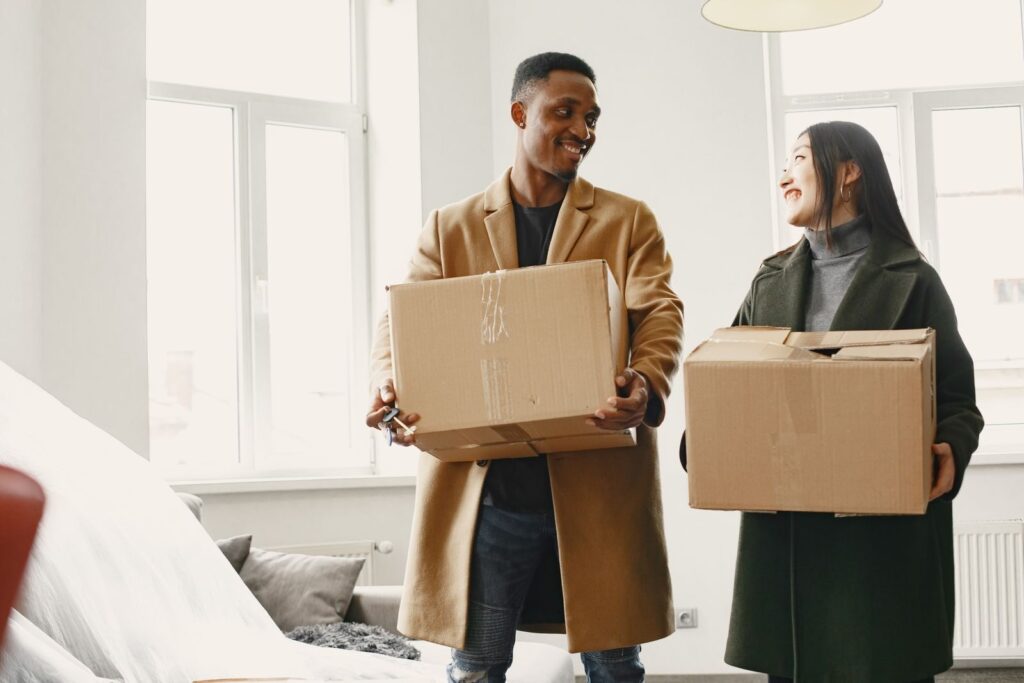 Happy couple carrying moving boxes into their new home, symbolizing a fresh start.